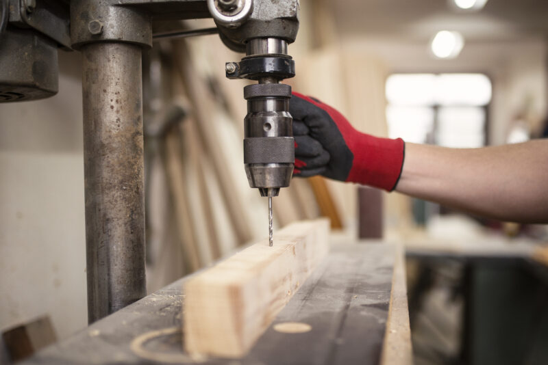 Carpentry workshop and drilling machine working on a piece of wood material.