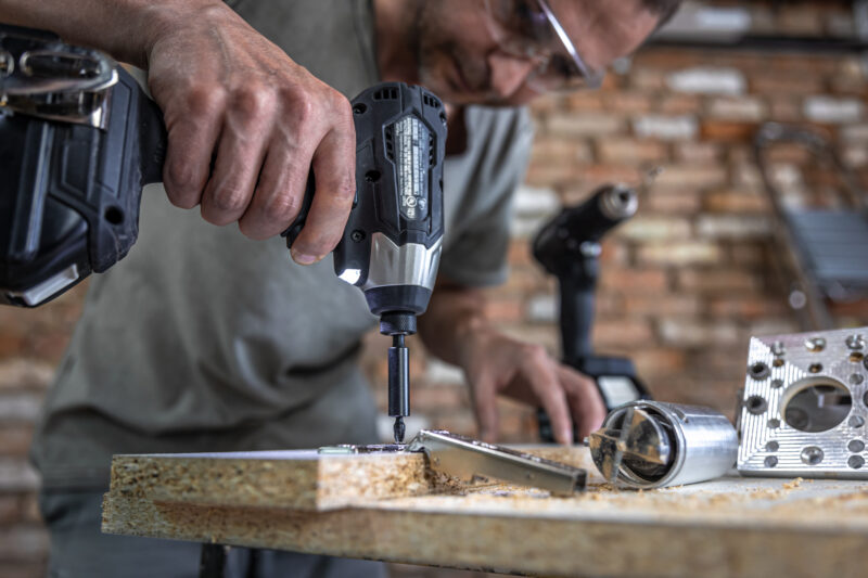 A man is screwing in a screw, a self tapping screw for wood.